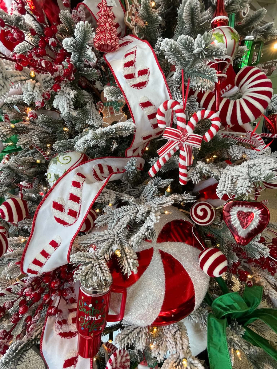 A close-up of a flocked Christmas tree decorated with red and white candy cane ornaments, white ribbons with red stripes, striped peppermint candies, red berries, and warm string lights.
